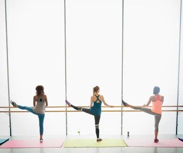 Women stretching at a barre in a bright fitness studio.