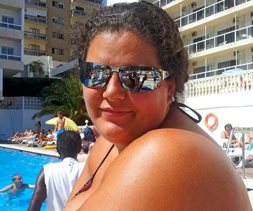 Person wearing sunglasses by a busy poolside, with buildings in the background.