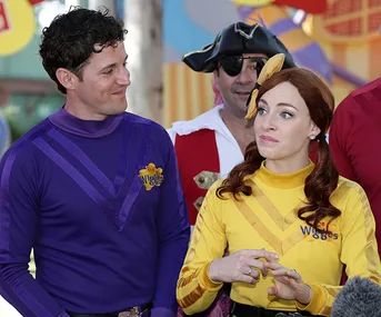 Two people in purple and yellow Wiggles costumes with a pirate character in the background.