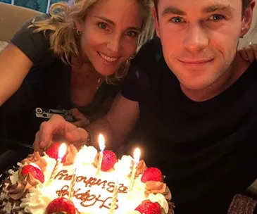 Man and woman pose with lit birthday cake topped with strawberries.