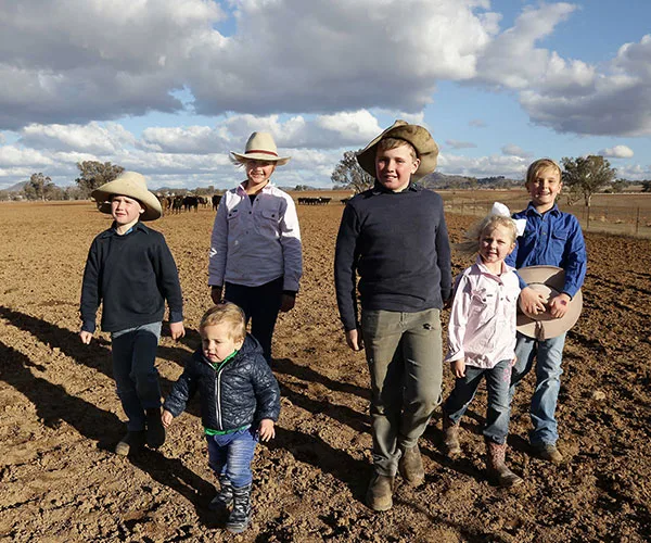 Children in cowboy hats standing on dry farmland under a partly cloudy sky in Australia.