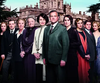 Cast of "Downton Abbey" standing in front of Highclere Castle, dressed in period costumes.