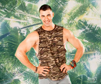 Man in a camouflage tank top poses with hands on hips, with a palm tree background.