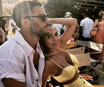 Couple sitting together at an outdoor event; man wearing sunglasses, woman in a yellow outfit.