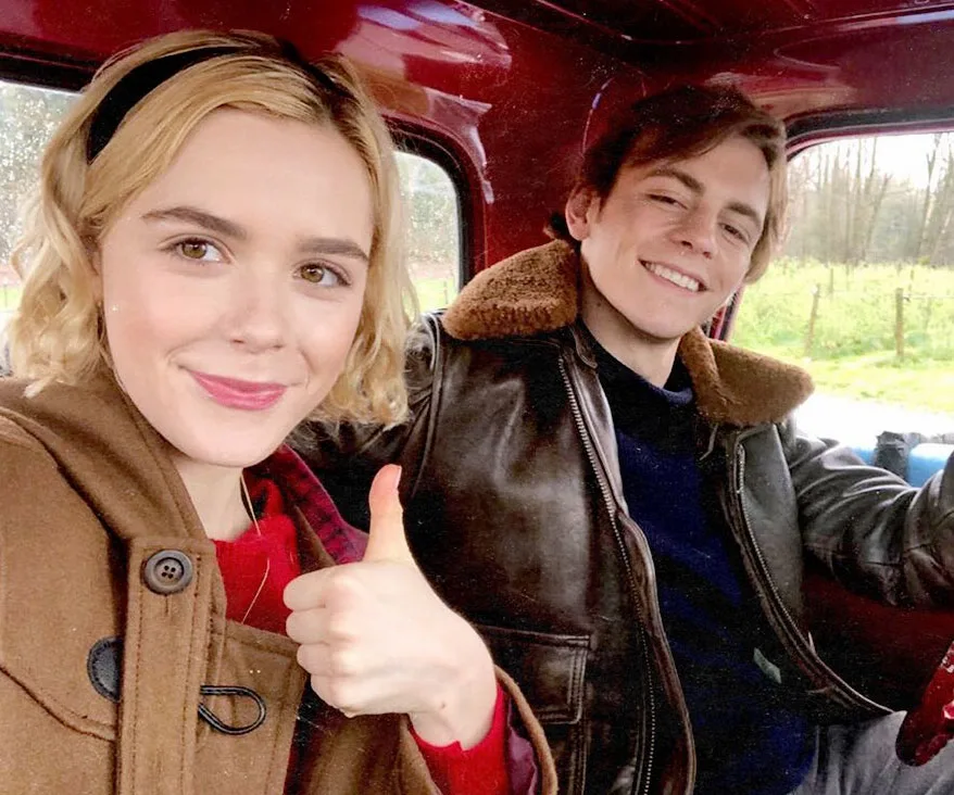 Two characters from the "Sabrina" reboot smiling in a car, one giving a thumbs-up.