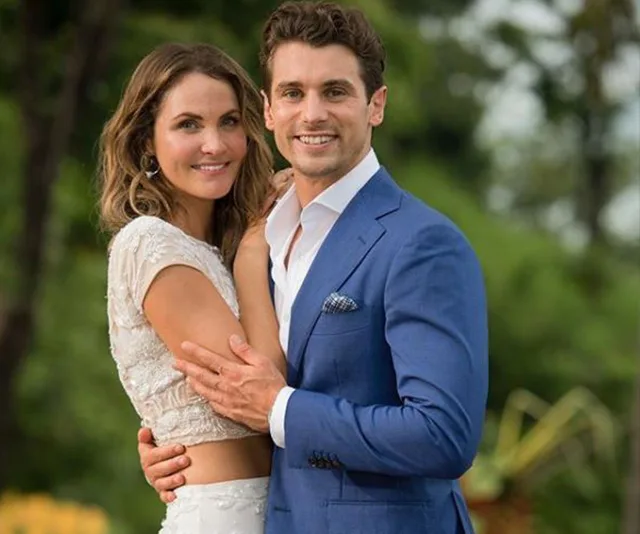 A couple embracing, smiling at the camera, outdoors in formal attire.