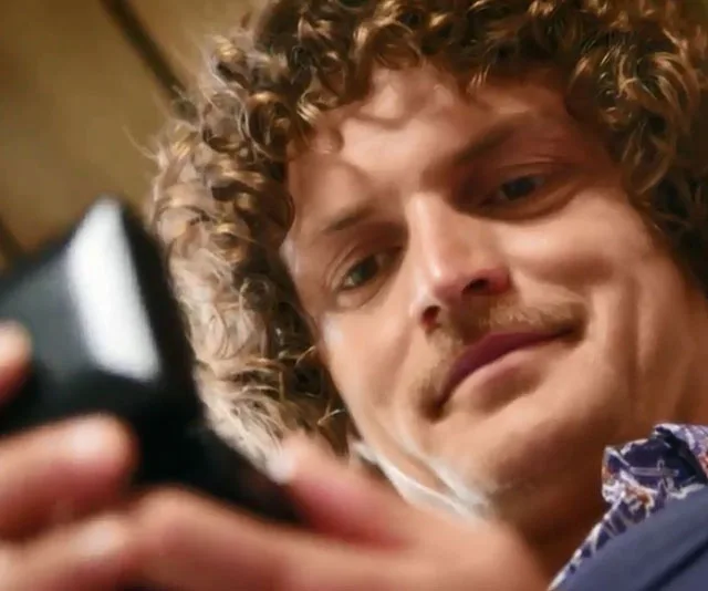 Nick Cummins smiling while looking at a phone, close-up shot.