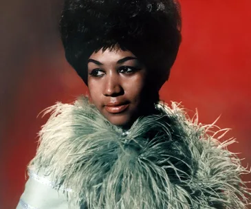 Portrait of a woman with a bouffant hairstyle and wearing a fur-trimmed outfit against a red background.