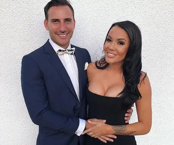 Couple posing in formal attire against a white background, man in blue suit, woman in black dress smiling.