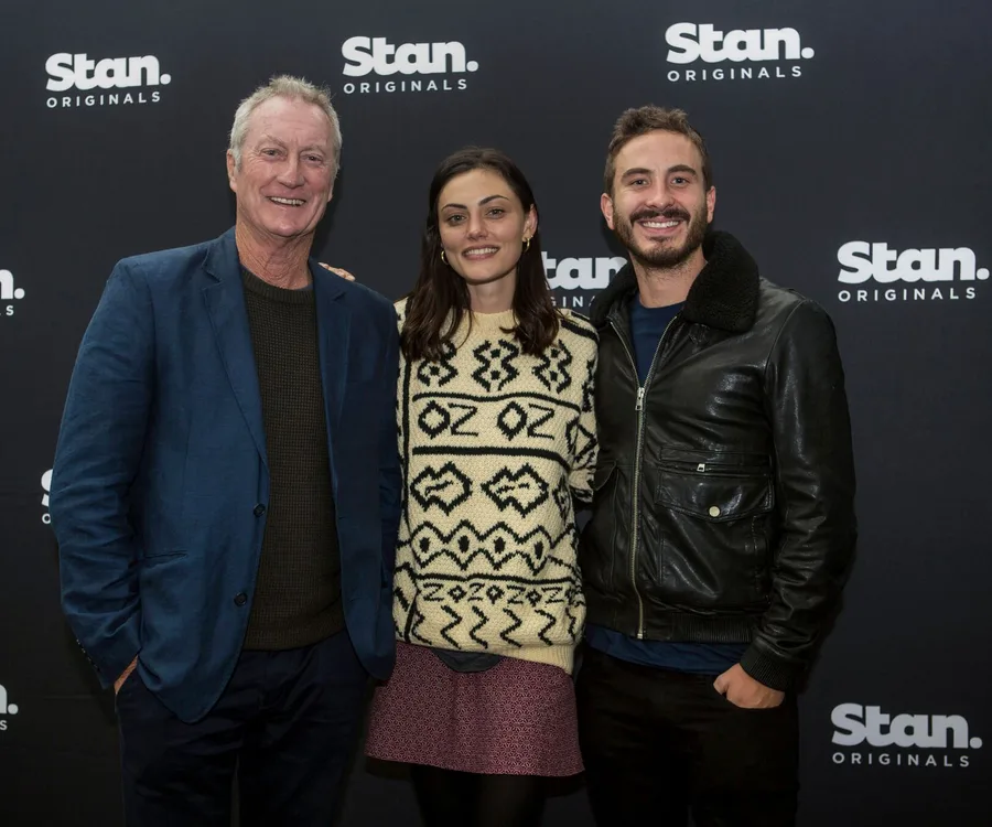 Three people smiling at a Stan Originals event, standing in front of a branded backdrop.