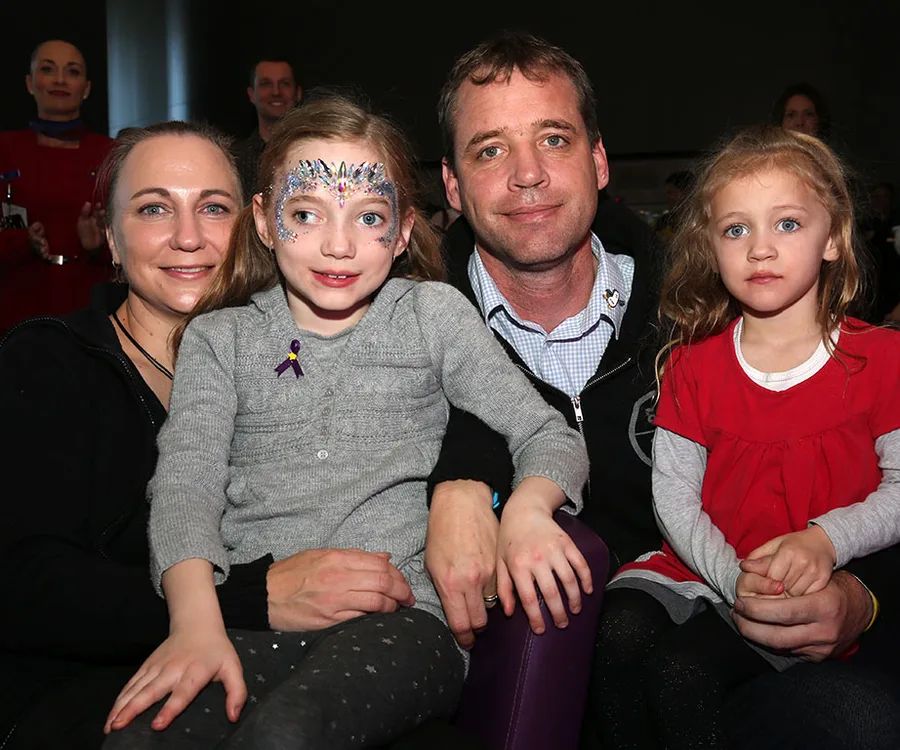 Family of four sitting together, young girl with face paint, wearing a gray sweater, surrounded by parents and sibling.