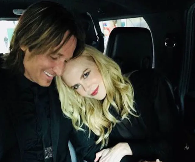 Couple sitting closely in a car, smiling while dressed in black outfits.