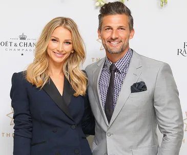 A smiling couple poses at an event, with a branded backdrop behind them.
