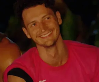 Benji Wilson from Survivor Australia smiles brightly in a pink shirt during an evening scene.