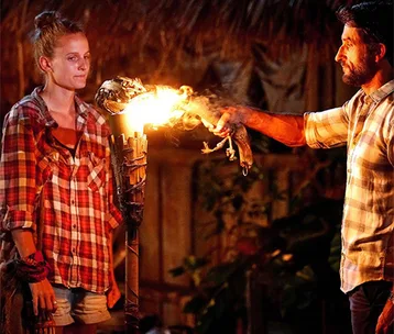 "Host extinguishing a contestant's torch in a dramatic tribal council setting on Survivor Australia."