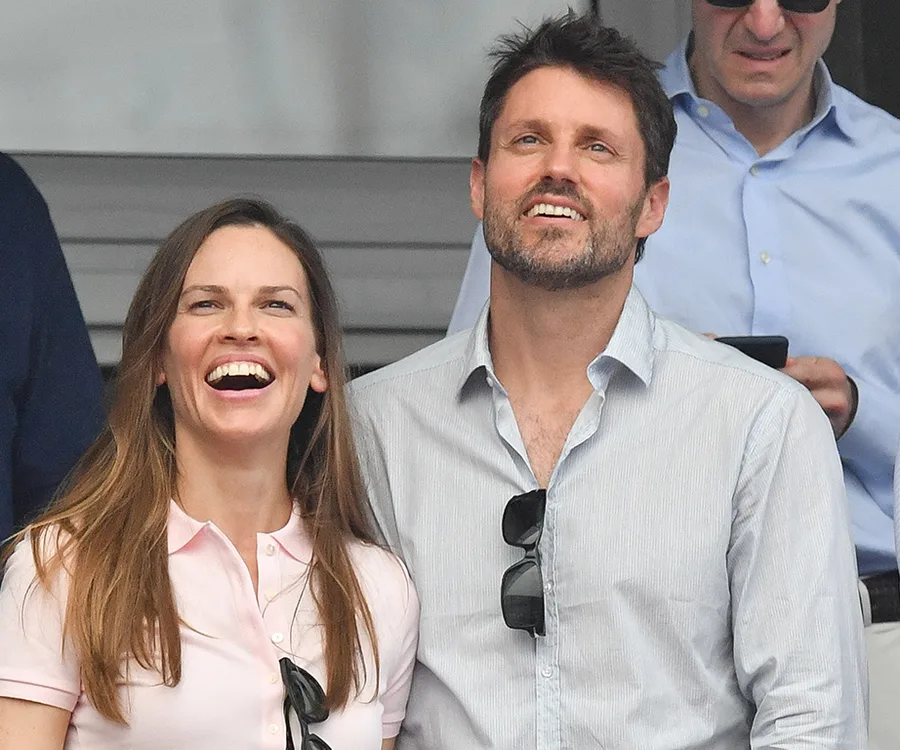 Two people smiling at an outdoor event, both wearing casual shirts, one with sunglasses hanging from the shirt.