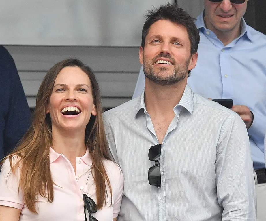 Two people smiling at an outdoor event, both wearing casual shirts, one with sunglasses hanging from the shirt.