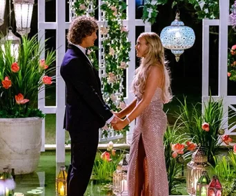 A couple holding hands in a romantic garden setting with lanterns and flowers at night.