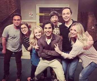 Cast of The Big Bang Theory smiling together on set in a casual group pose.