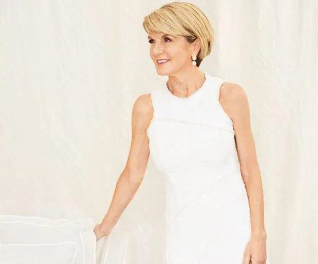 A woman in a white dress standing and smiling against a white background.
