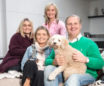 A smiling family sitting together, one holding a TV Week Logie Award, another holding a fluffy dog, in a cozy home setting.