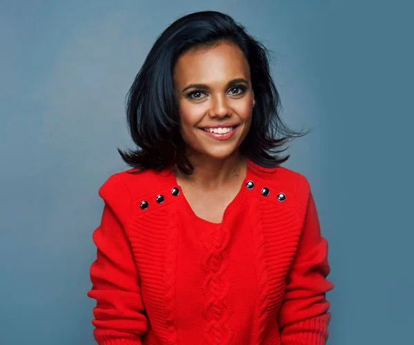 Smiling woman with dark hair in a red sweater against a gray background.