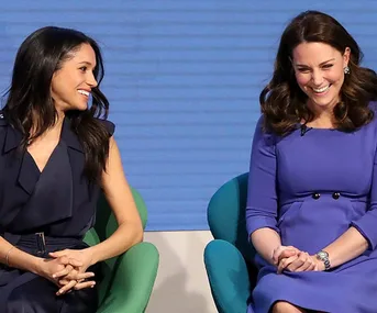 Two women seated, smiling and looking at each other, attending an event together.