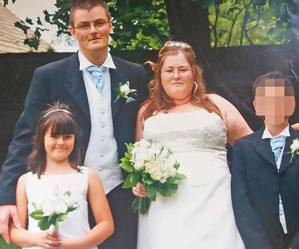 Wedding photo of a couple with a bouquet, a young girl and a boy with a pixelated face, outdoors.