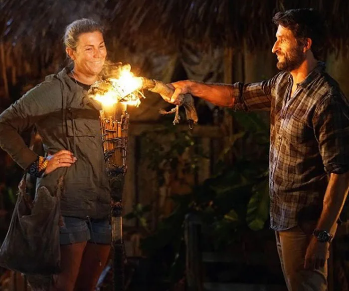 Jackie Glazier at a torch extinguishing ceremony during Australian Survivor, standing with a host in tribal setting.