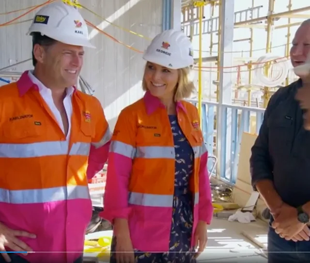 Karl and Georgie in orange safety gear and hard hats at a construction site with a colleague.