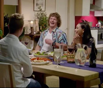Contestants on "The Bachelor" 2018 share a cheerful dinner, with laughter around a table set with food and drinks.