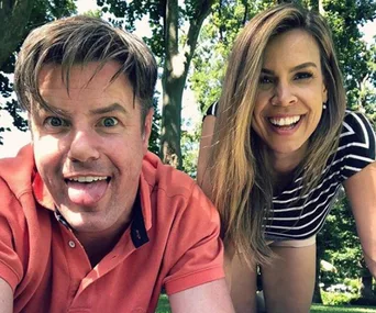 Two people smiling and posing playfully outdoors with trees in the background.
