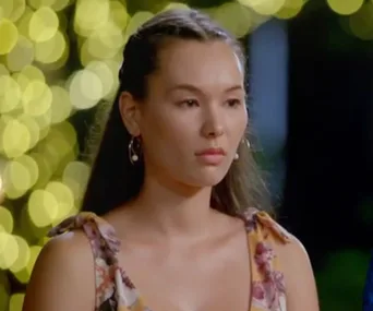 Vanessa Sunshine at a rose ceremony on "The Bachelor," wearing a floral dress and earrings, with blurred lights in the background.