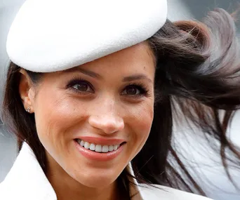 A smiling woman in a white hat with flowing hair.
