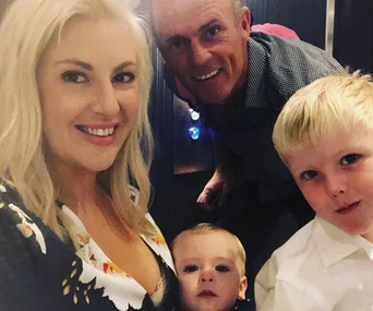 Family of four smiling: mother, father, and two young children, with a background of an elevator interior.