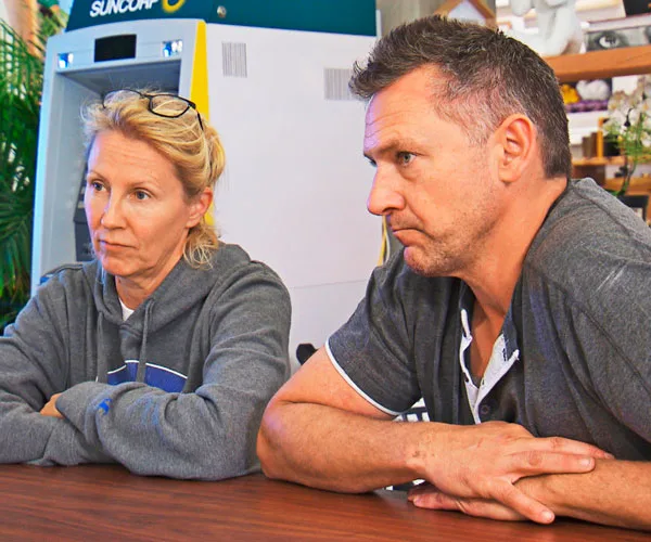 Couple sitting at a table looking serious; both wearing casual clothing.