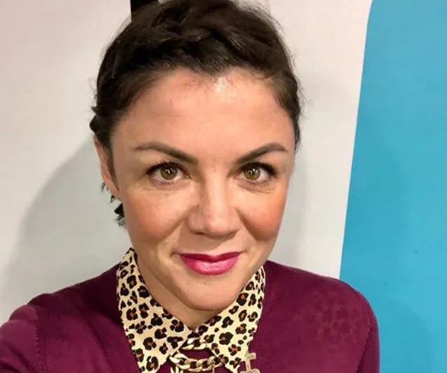 A woman with braided hair, wearing a leopard print collar shirt and purple sweater, smiling at the camera.