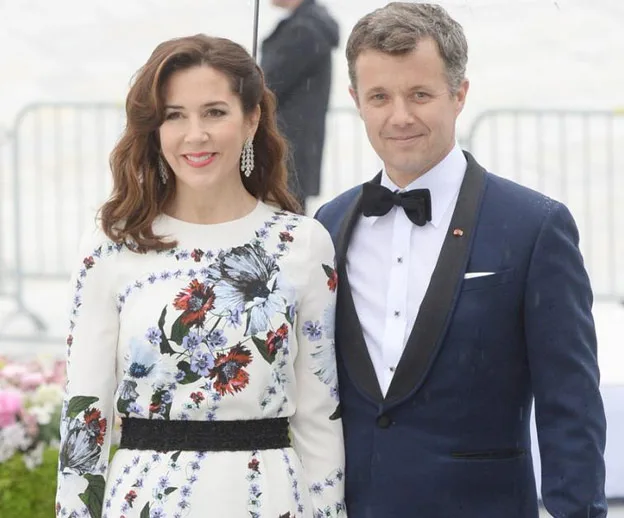 A man in a tuxedo and a woman in a floral dress smile together outdoors.