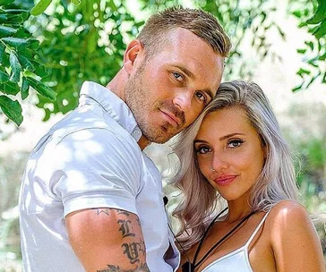 Couple posing together outdoors with lush greenery in the background.