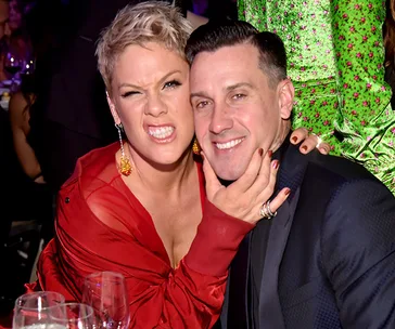 A woman in a red outfit playfully embraces a man in a dark suit at a lively indoor event.