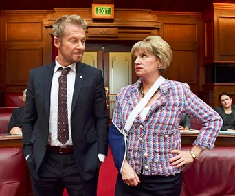 Two characters in a courtroom, one with an injured arm in a sling, engaging in intense conversation.