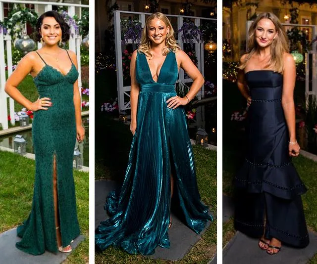 Three women in elegant formal gowns at an outdoor event, standing on grass with floral decor in the background.