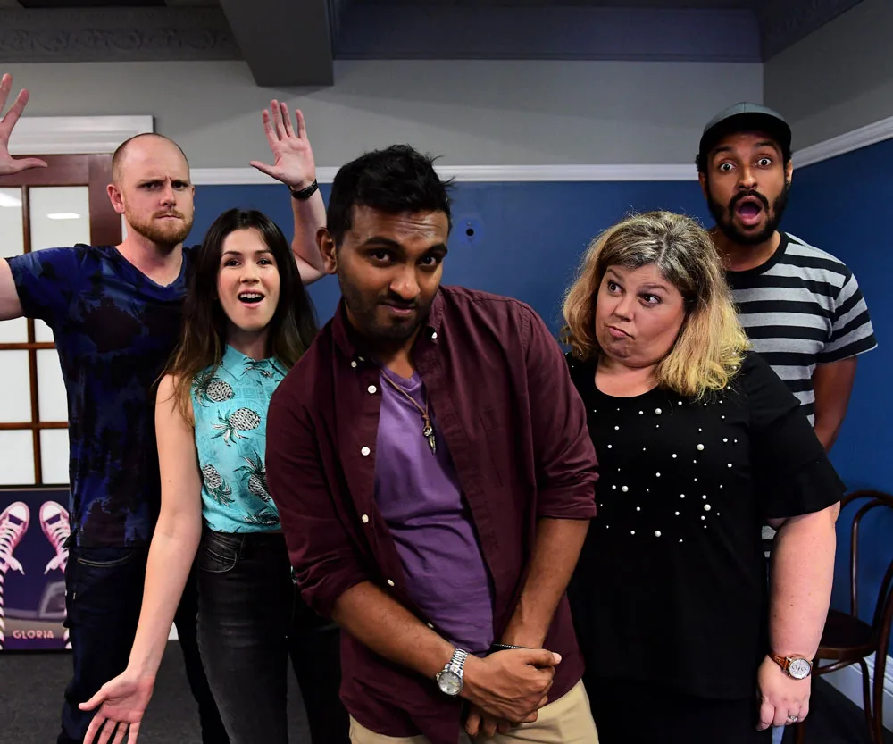 Comedy show cast posing playfully with various expressions against a blue wall.
