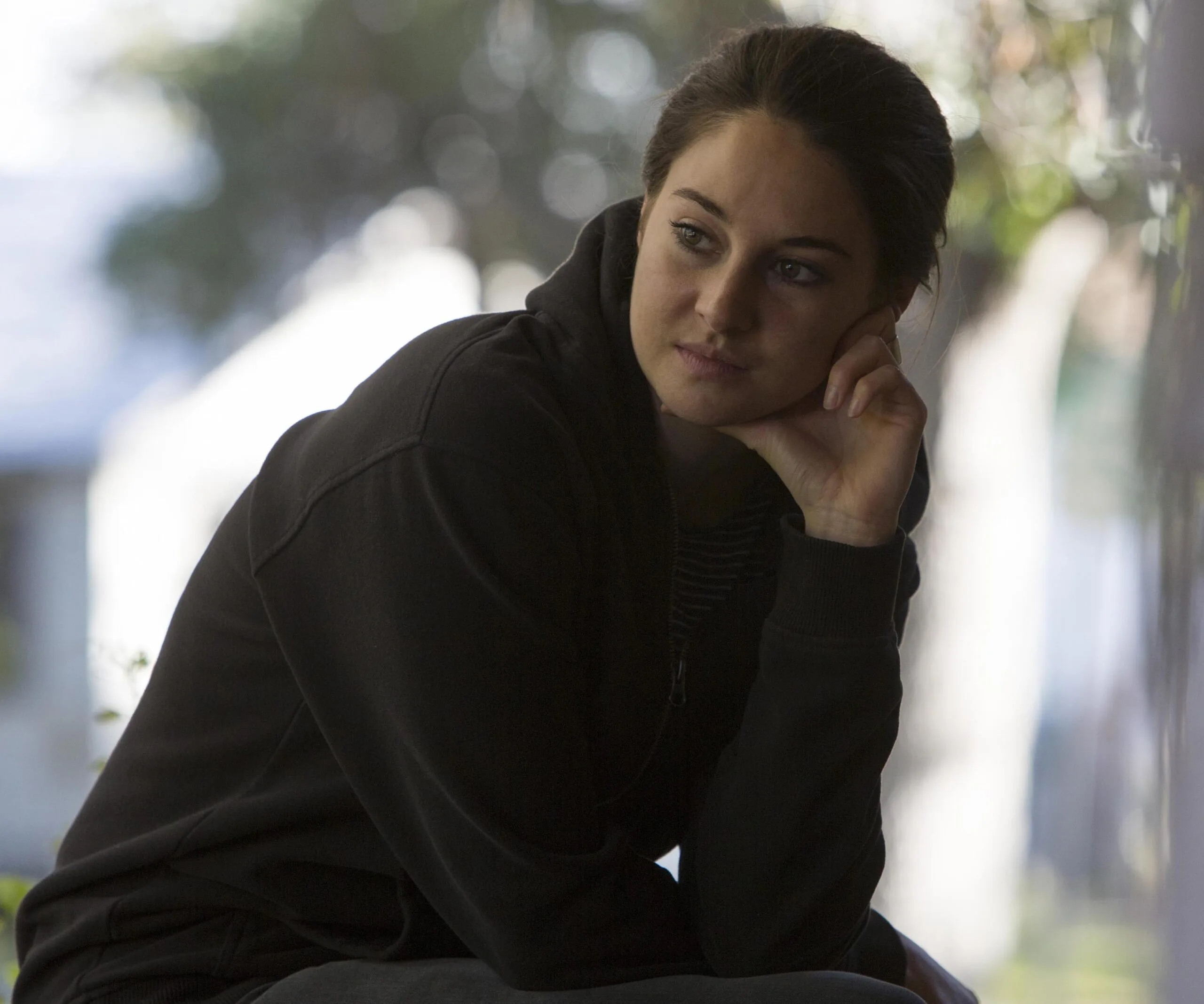 Woman in a black jacket sitting thoughtfully, resting her head on her hand, outdoors.