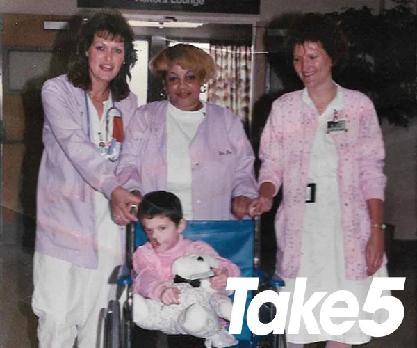 Hospital staff with a child in wheelchair holding a plush toy, Take5 magazine logo at the corner.