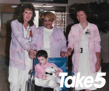 Hospital staff with a child in wheelchair holding a plush toy, Take5 magazine logo at the corner.