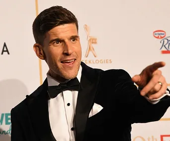 Man in a tuxedo pointing, on a red carpet at an awards event.