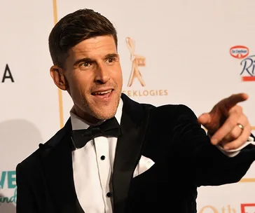 Man in a tuxedo pointing, on a red carpet at an awards event.