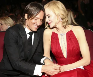 Couple sitting together at an event, dressed formally and holding hands, sharing a tender moment.