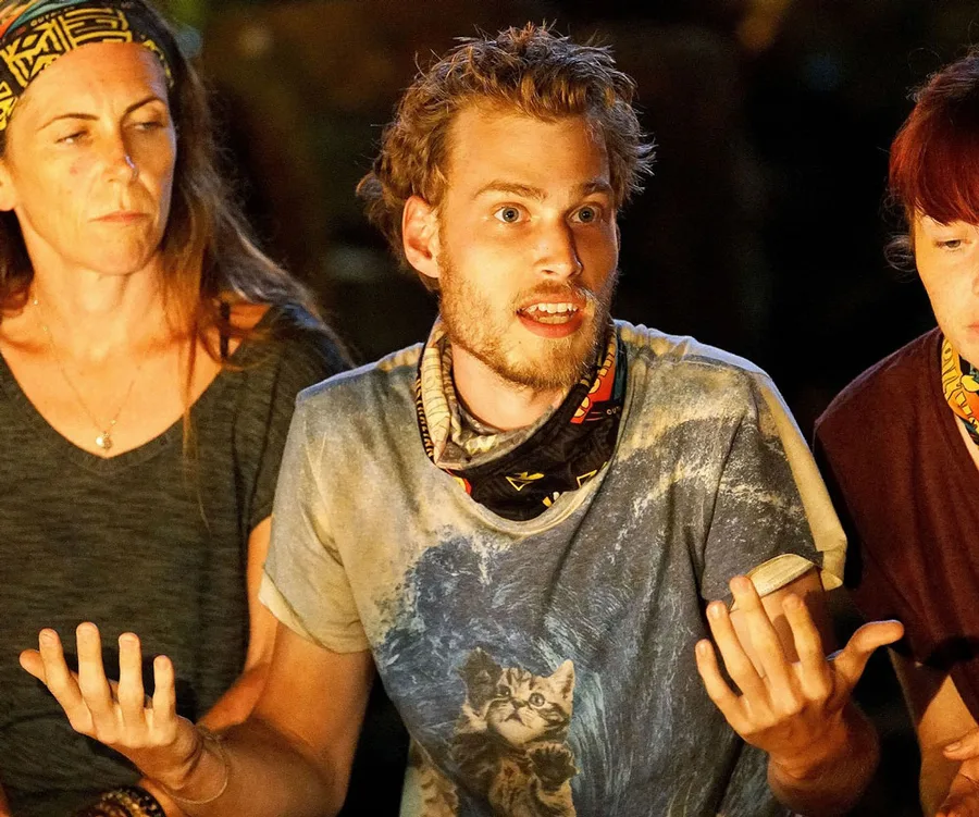 "Three people at a tense discussion on Australian Survivor, one with a cat print shirt gesturing animatedly."